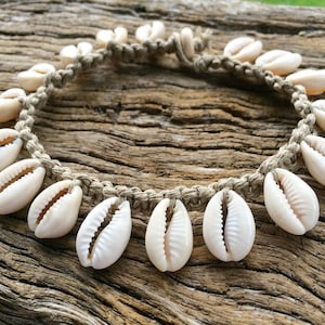 May include: A white shell necklace with a natural jute cord. The necklace is made with cowrie shells and has a simple design.