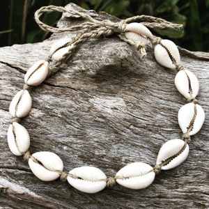 May include: A white shell necklace with a natural rope closure. The necklace is made of cowrie shells and is tied together with a natural rope.
