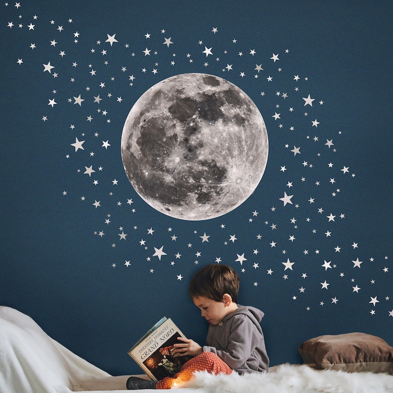 Puede incluir: Un ni&ntilde;o est&aacute; sentado en una alfombra blanca leyendo un libro titulado "Dersou Uzala, Grand Nord" frente a una pared azul con una gran luna gris y estrellas blancas.