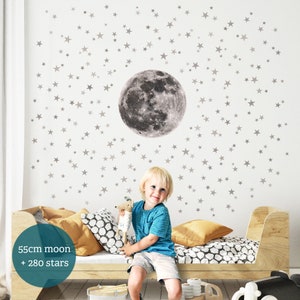 Puede incluir: Un ni&ntilde;o se sienta en una cama con una luna gris y 280 estrellas blancas en pegatinas de pared. La luna tiene un di&aacute;metro de 55 cm. Las pegatinas est&aacute;n en una pared blanca.