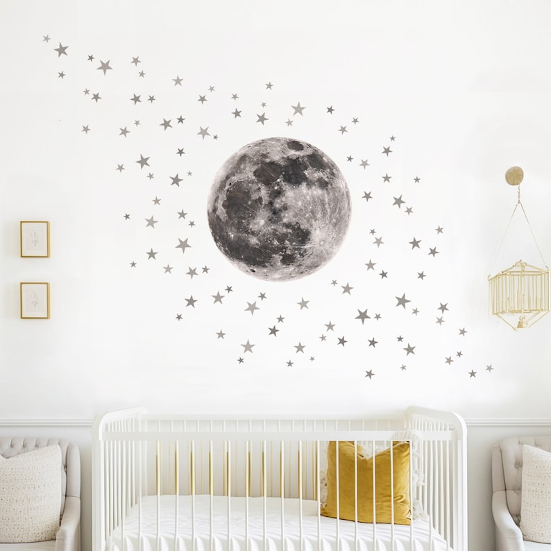 Puede incluir: Una cuna blanca con una almohada amarilla y una pared blanca con una gran luna gris y muchas peque&ntilde;as estrellas grises.