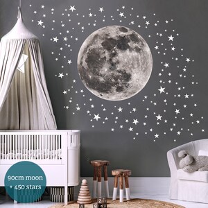 Puede incluir: Una habitaci&oacute;n de beb&eacute; con una pared gris decorada con una gran luna gris y 450 estrellas blancas. La habitaci&oacute;n tambi&eacute;n cuenta con una cuna blanca, un dosel blanco y dos taburetes de madera.