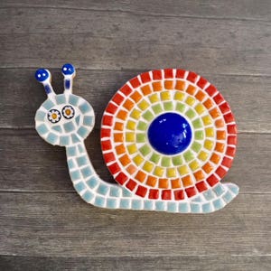 May include: A mosaic snail with a rainbow shell and blue eyes. The snail's shell is made of small, colorful tiles arranged in a circular pattern.