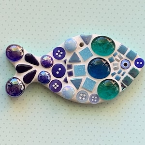May include: A mosaic fish made of blue, green, and purple glass tiles. The fish is white and has a black outline.