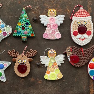 May include: Nine handmade Christmas ornaments made of mosaic tiles. The ornaments include a stocking, a Christmas tree, an angel, Santa Claus, a reindeer, a bird, a star, and a round ornament. The ornaments are all decorated with colorful tiles and buttons.