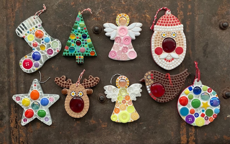 May include: Nine handmade Christmas ornaments made of mosaic tiles. The ornaments include a stocking, a Christmas tree, an angel, Santa Claus, a reindeer, a bird, a star, and a round ornament. The ornaments are all decorated with colorful tiles and buttons.