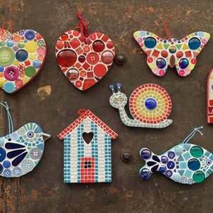 May include: A collection of eight mosaic ornaments, including a heart, a butterfly, a snail, a house, a bird, a fish, and an ice cream cone. The ornaments are made with colorful glass tiles and buttons.