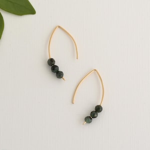 May include: A pair of gold earrings with three dark green gemstone beads on each earring.