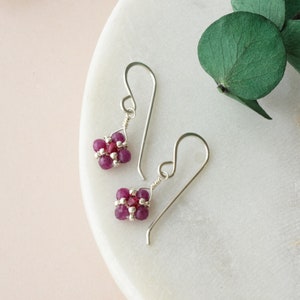 May include: A pair of silver earrings with small pink gemstone clusters. The earrings have a simple, delicate design.