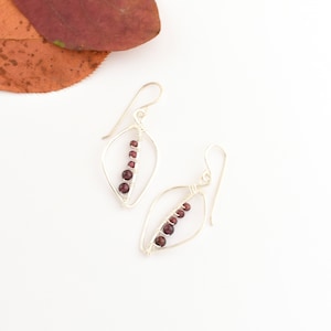 May include: Silver wire earrings with a leaf design and a row of dark red garnet beads.