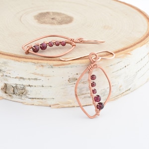 May include: A pair of copper wire earrings with a teardrop shape and a line of small, dark red garnet beads.