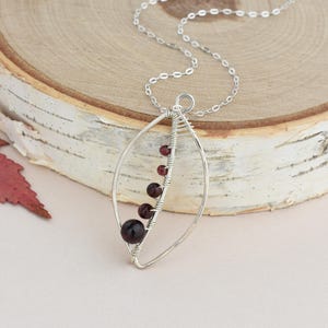 May include: A silver chain necklace with a pendant featuring a silver wire wrapped oval shape with a line of dark red garnet gemstones.