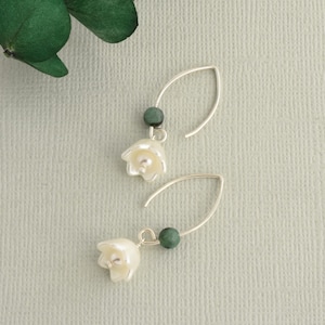 May include: A pair of silver earrings with a white flower charm and a green gemstone bead.