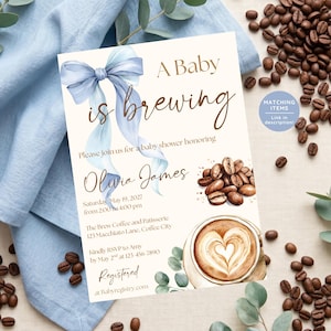 May include: Baby shower invitation with the text "A Baby is Brewing" and details for Olivia James's baby shower. The design features a blue ribbon, coffee beans, and a latte with heart art. Eucalyptus sprigs and coffee beans surround the invitation.