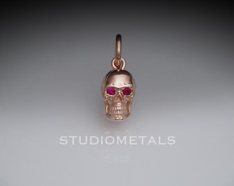 May include: A gold skull pendant with red gemstone eyes. The pendant is a detailed depiction of a human skull.