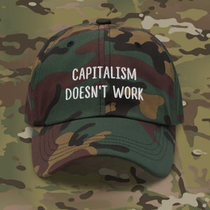 May include: A camouflage green baseball cap with the text "Capitalism Doesn't Work" embroidered in white.