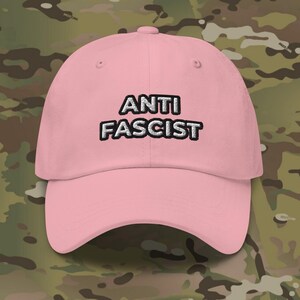 Könnte beinhalten: Eine rosafarbene Baseballkappe mit dem Schriftzug "ANTI FASCIST", der in Weiß auf der Vorderseite gestickt ist.