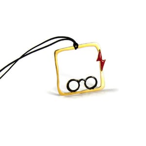 Könnte beinhalten: Eine goldene Halskette mit einem quadratischen Anhänger, der eine runde Brille und einen roten Blitz zeigt.