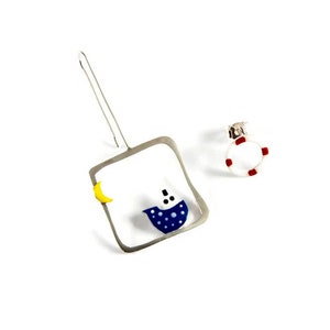 Peut inclure: Une paire de boucles d'oreilles en argent avec un bateau bleu et blanc, une lune croissante jaune et une bouée de sauvetage rouge et blanche.