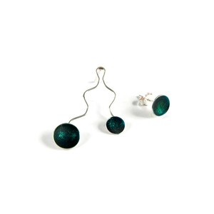 May include: A jewelry set featuring a pendant and stud earrings. The pendant has two dark teal, glittery circular pendants connected by a silver, wavy wire. The stud earrings have a similar design. All pieces are set against a white background.