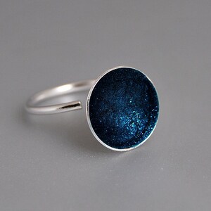 May include: A silver ring with a round, dark blue enamel top. The enamel has a sparkly, textured finish.