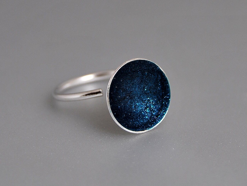 May include: A silver ring with a round, dark blue enamel top. The enamel has a sparkly, textured finish.
