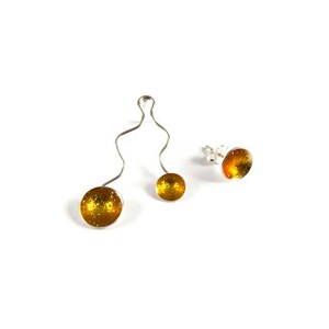 May include: A set of three pieces of jewelry: a pair of earrings and a pendant. The earrings are stud style with a silver post and a round, glittery, amber-colored stone. The pendant has a silver wire design with two amber-colored glittery spheres.
