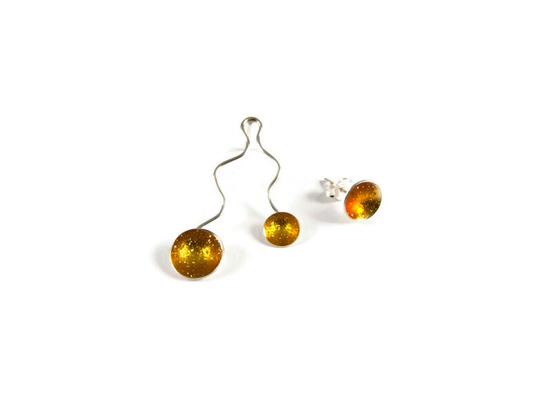 May include: A set of three pieces of jewelry: a pair of earrings and a pendant. The earrings are stud style with a silver post and a round, glittery, amber-colored stone. The pendant has a silver wire design with two amber-colored glittery spheres.