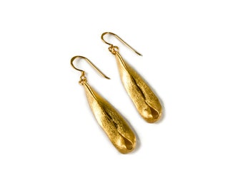 Puede incluir: Un par de pendientes de color dorado con una forma única de lágrima. Los pendientes están hechos de metal texturizado y tienen un acabado liso y pulido.