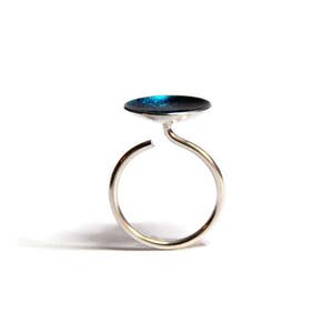 May include: A silver ring with a blue enamel top. The ring is open and has a simple design.
