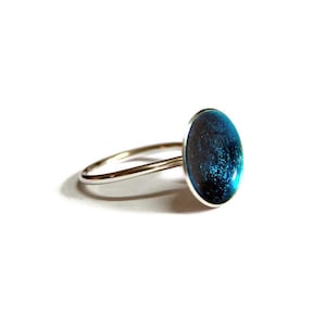 May include: A silver ring with a blue oval-shaped stone set in the center. The stone has a sparkly, glittery finish.