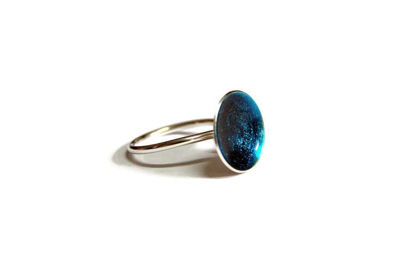 May include: A silver ring with a blue oval-shaped stone set in the center. The stone has a sparkly, glittery finish.