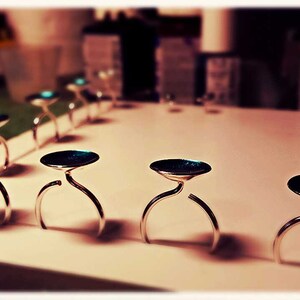 May include: A row of silver ring holders with teal blue tops. The holders are arranged on a white surface.