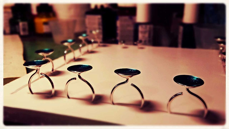 May include: A row of silver ring holders with teal blue tops. The holders are arranged on a white surface.