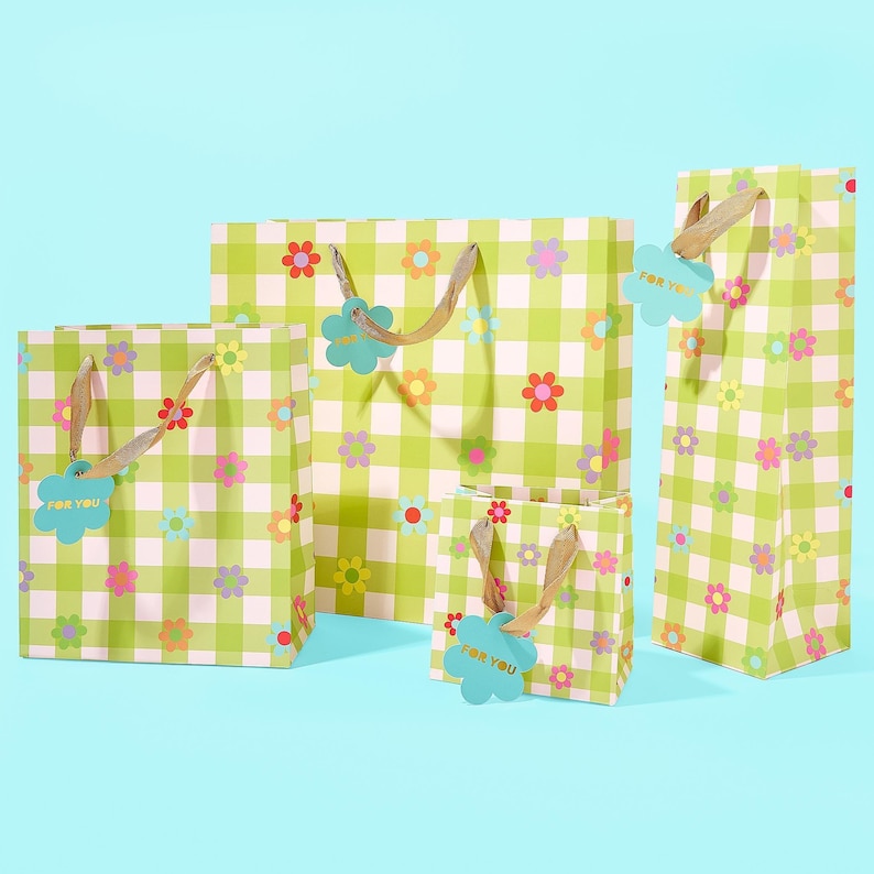 May include: A collection of gift bags in various sizes, featuring a green and white checkered pattern adorned with colorful flower designs. Each bag has a light brown handle and a blue tag that says "FOR YOU".
