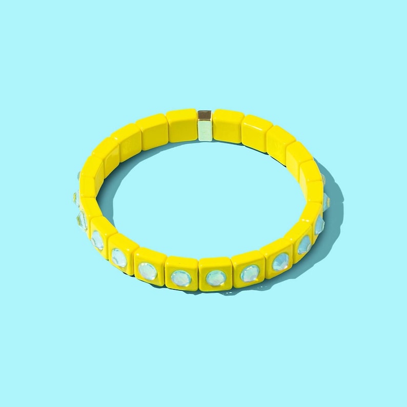 May include: A yellow bracelet with clear iridescent stones. The bracelet is made of square beads and has a metal clasp.