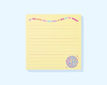 Puede incluir: Un bloc de notas amarillo con líneas y el texto "BE THE HYPE GIRL YOU WISH TO SEE IN THE WORLD" en rosa, azul y verde. Un gráfico de bola de discoteca colorida está en la esquina inferior derecha. El bloc de notas está sobre un fondo azul claro.