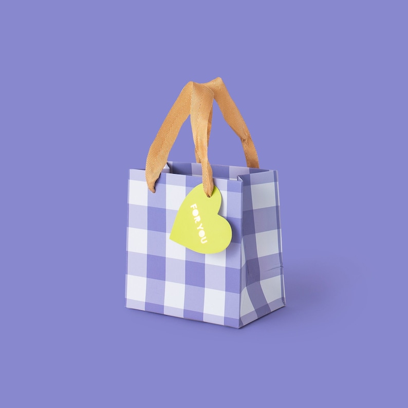 May include: A small gift bag with a purple and white checkered pattern. The bag has gold-colored handles and a heart-shaped tag that says "FOR YOU" in yellow. The background is a solid purple.