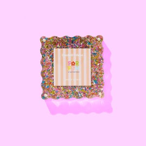 May include: A square picture frame with a scalloped edge, speckled with colourful confetti. The frame holds a card with the text "Confetti Frame" and "FOR FUN" on a striped background. The frame is on a pink background.