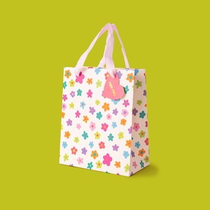 May include: A white gift bag with a pink handle and a pink heart-shaped tag that says "For You". The bag is covered in a pattern of colourful flowers.