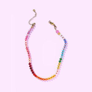 May include: A colorful beaded necklace with a rainbow gradient. The necklace features small, round beads in shades of red, orange, yellow, green, blue, and purple. The necklace has a gold-colored chain and clasp.