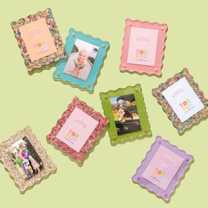 May include: A collection of colorful, glitter-framed photo holders. Each frame holds a small photo and a card with the text "FOR FUN". The frames are in various colors, including pink, green, blue, and purple, with a wavy edge design.