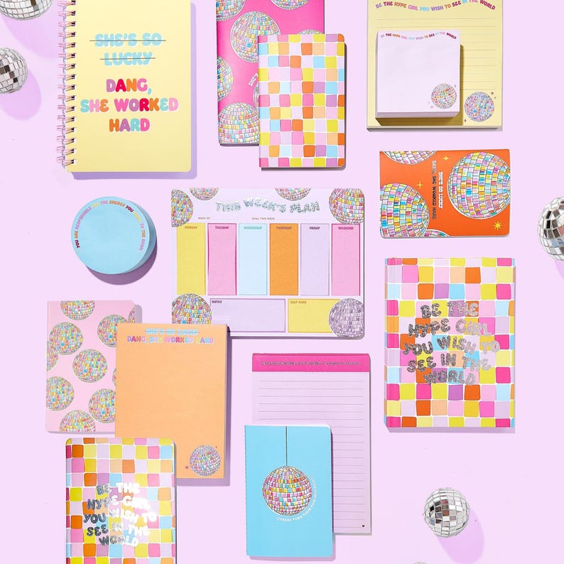 May include: A collection of stationery items, including notebooks, notepads, and sticky notes, in various sizes and colors. The items feature disco ball and grid patterns, with text like "She's so lucky" and "Be the hope you wish to see in the world."