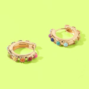Pair of gold hoop earrings with colorful stones on a green background