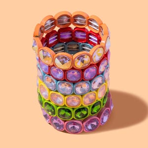 Puede incluir: Una pila de pulseras coloridas con cristales de forma cuadrada. Las pulseras son de diferentes colores, incluyendo naranja, rojo, morado, azul, amarillo, verde y rosa.