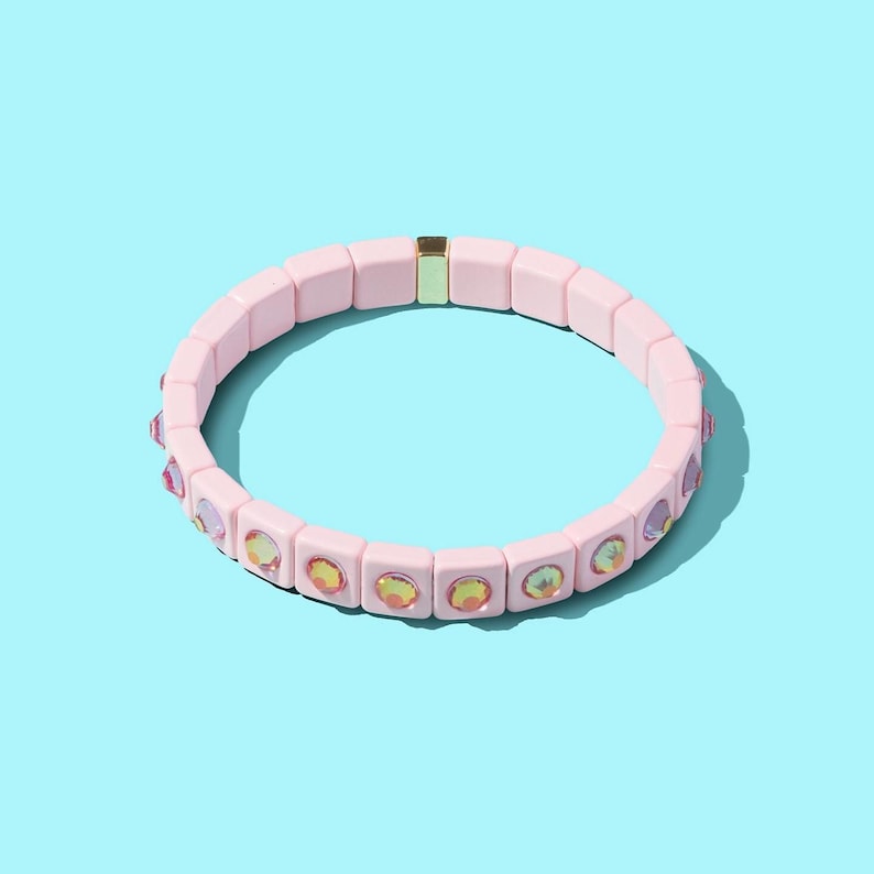 May include: A pink beaded bracelet with iridescent rhinestones. The bracelet is made of square beads and has a gold clasp.