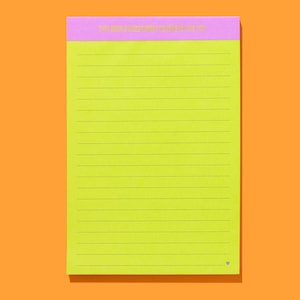 Op de afbeelding: Een neon groen notitieblok met horizontale lijnen en een roze kop. De kop luidt "THIS WORLD NEEDS MORE SERIOUSLY YOU". Het notitieblok staat op een oranje achtergrond.