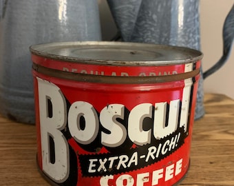 May include: A vintage red and white Boscul Extra-Rich Coffee tin with the words "Boscul" and "Extra-Rich Coffee" in white lettering. Two gray enamelware coffee pots are in the background. The tin is on a wooden surface.