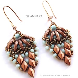 Puede incluir: Un par de pendientes de cuentas de cobre y turquesa con un diseño geométrico. Los pendientes están hechos con pequeñas cuentas de semillas y cuentas de cobre más grandes. Los pendientes cuelgan de un gancho de alambre de cobre.