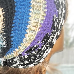 May include: A colorful crocheted hat with a long, striped tail. The hat is made of various colors, including black, white, blue, purple, and beige. The tail is also striped and has a fluffy texture.